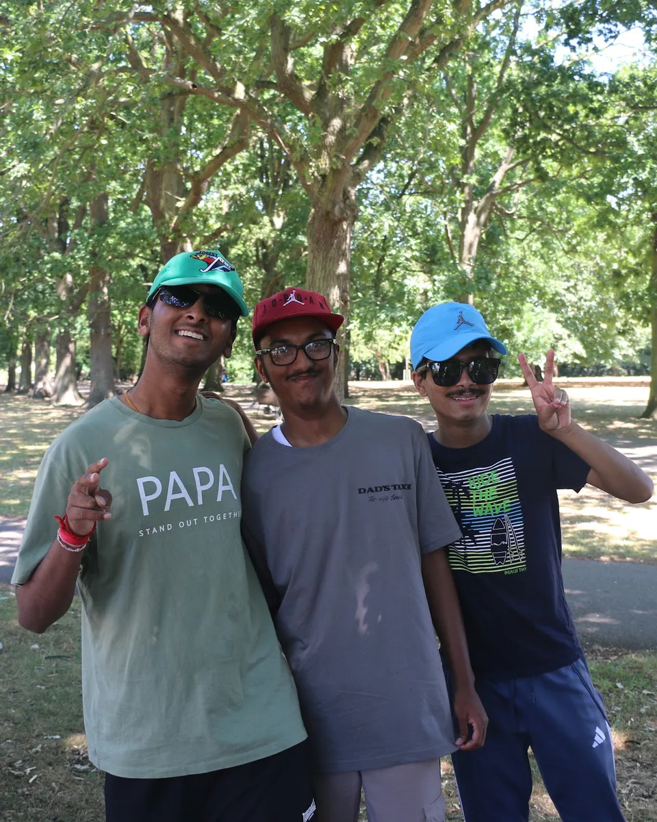 Three young men arm in arm, smiling, at the TSC charity walk in the park.